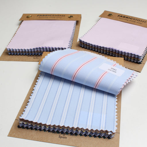 Three fabric swatch booklets on brown cardboard hangers, showing folded fabric samples in pastel pink and light blue with white stripes on a white background.